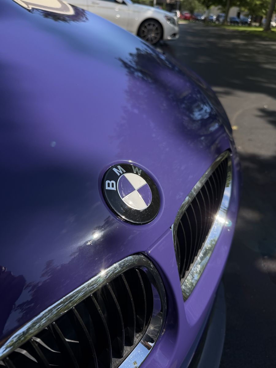 Close-up of the BMW roundel on the hood of a purple wrapped M3, kidney grille below