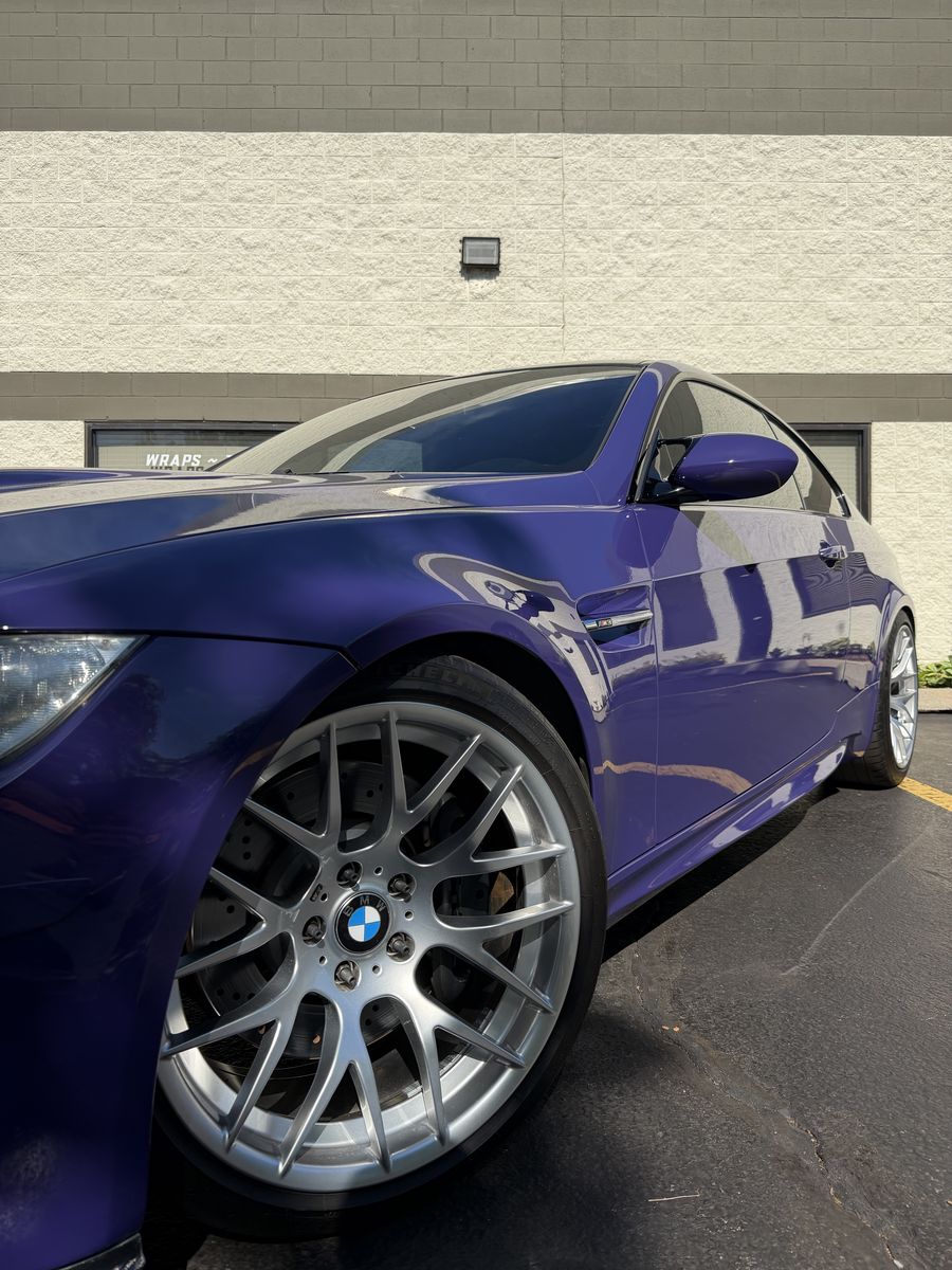 Front three-quarter of a purple wrapped BMW M3, forged wheel in the foreground