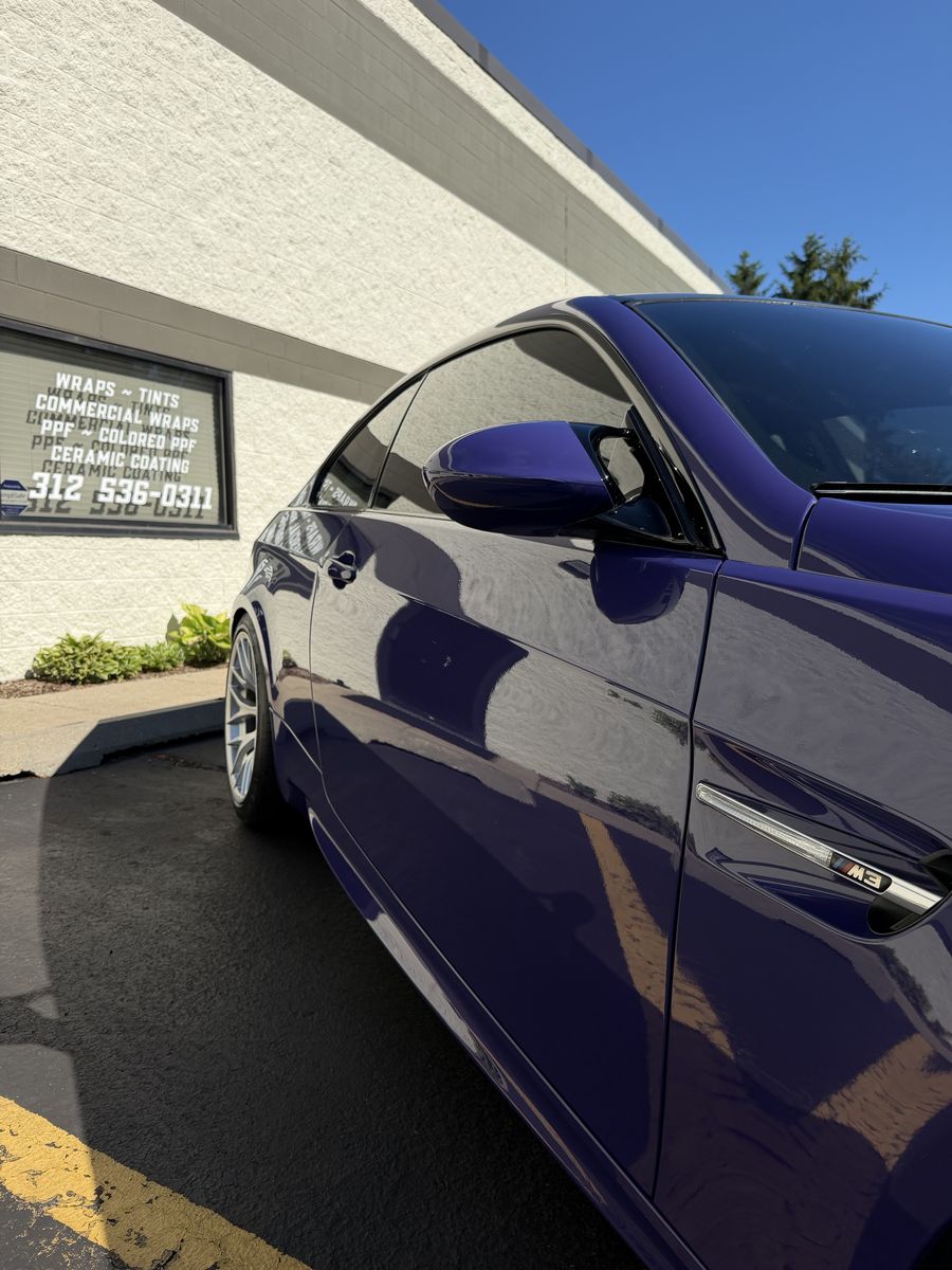 Purple wrapped BMW M3 along its side, parked outside the shop