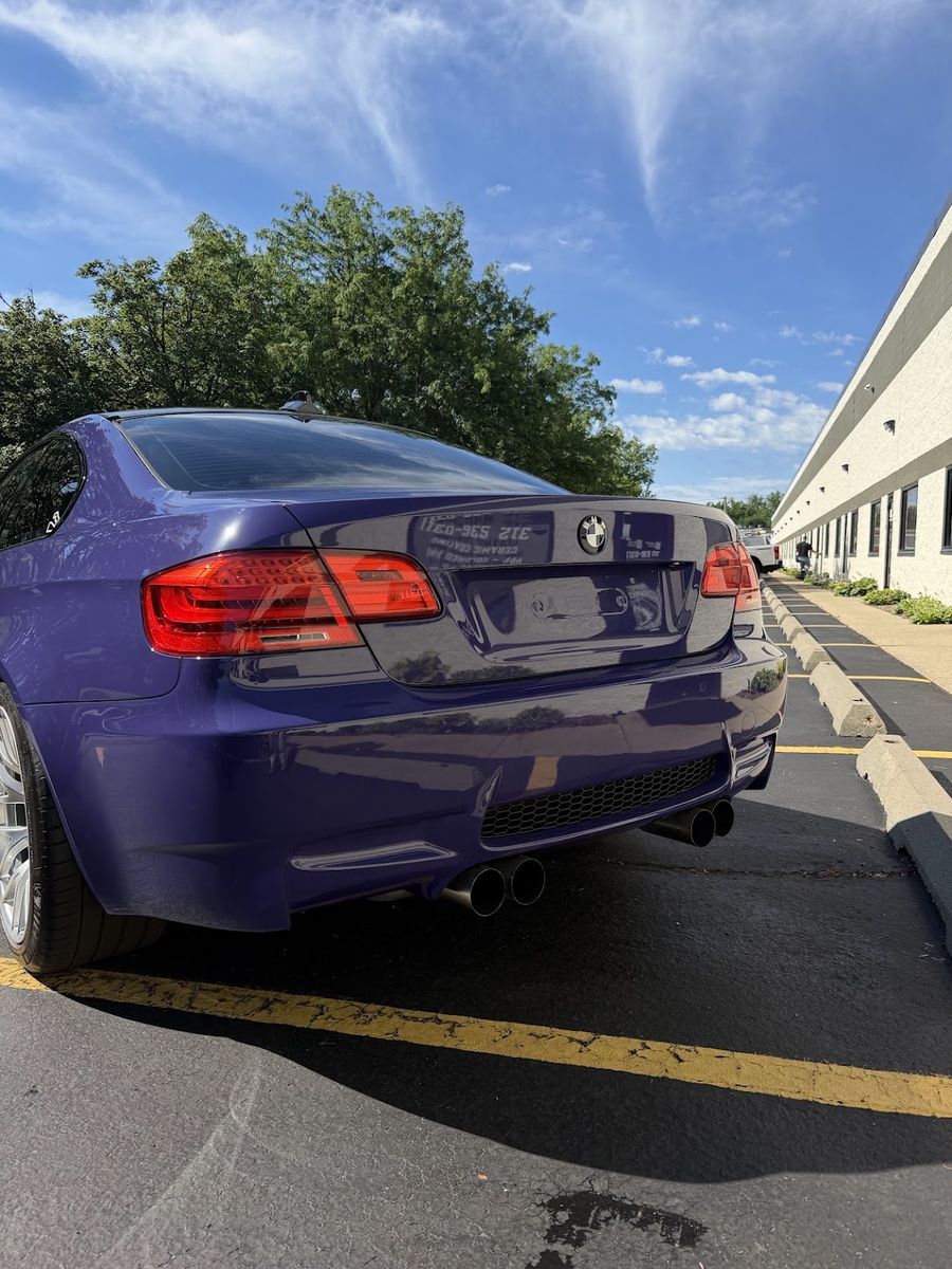 Rear of a purple wrapped BMW M3, quad exhaust and diffuser under a clear sky