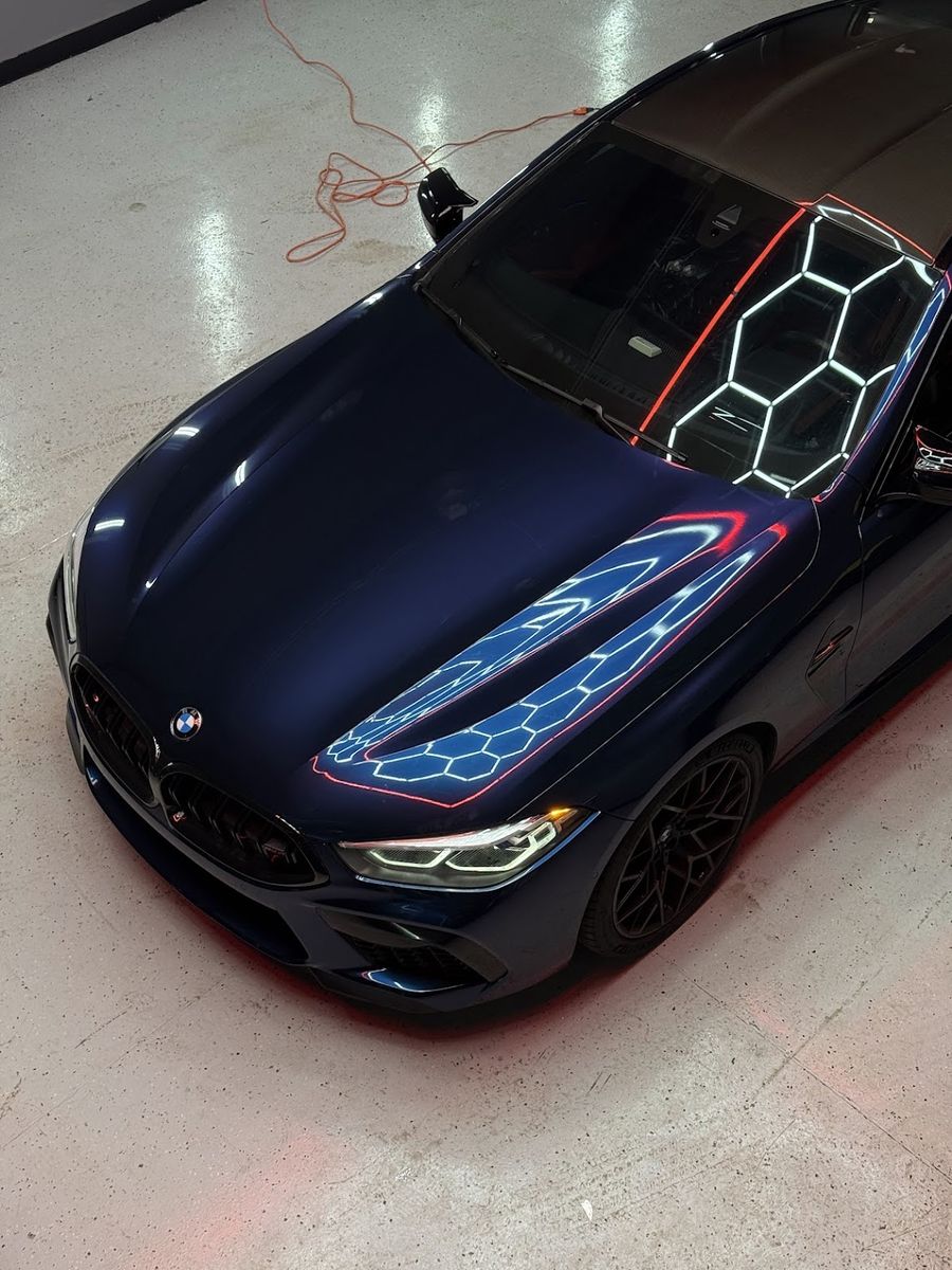 Overhead view of a navy BMW M8, hex lighting reflected across the hood