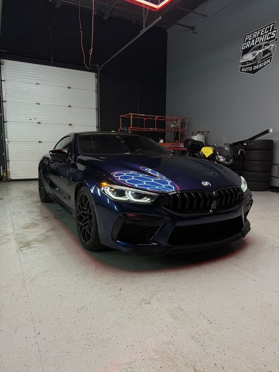 BMW M8 wrapped in navy blue, inside the Perfect Graphics shop under the hex lights