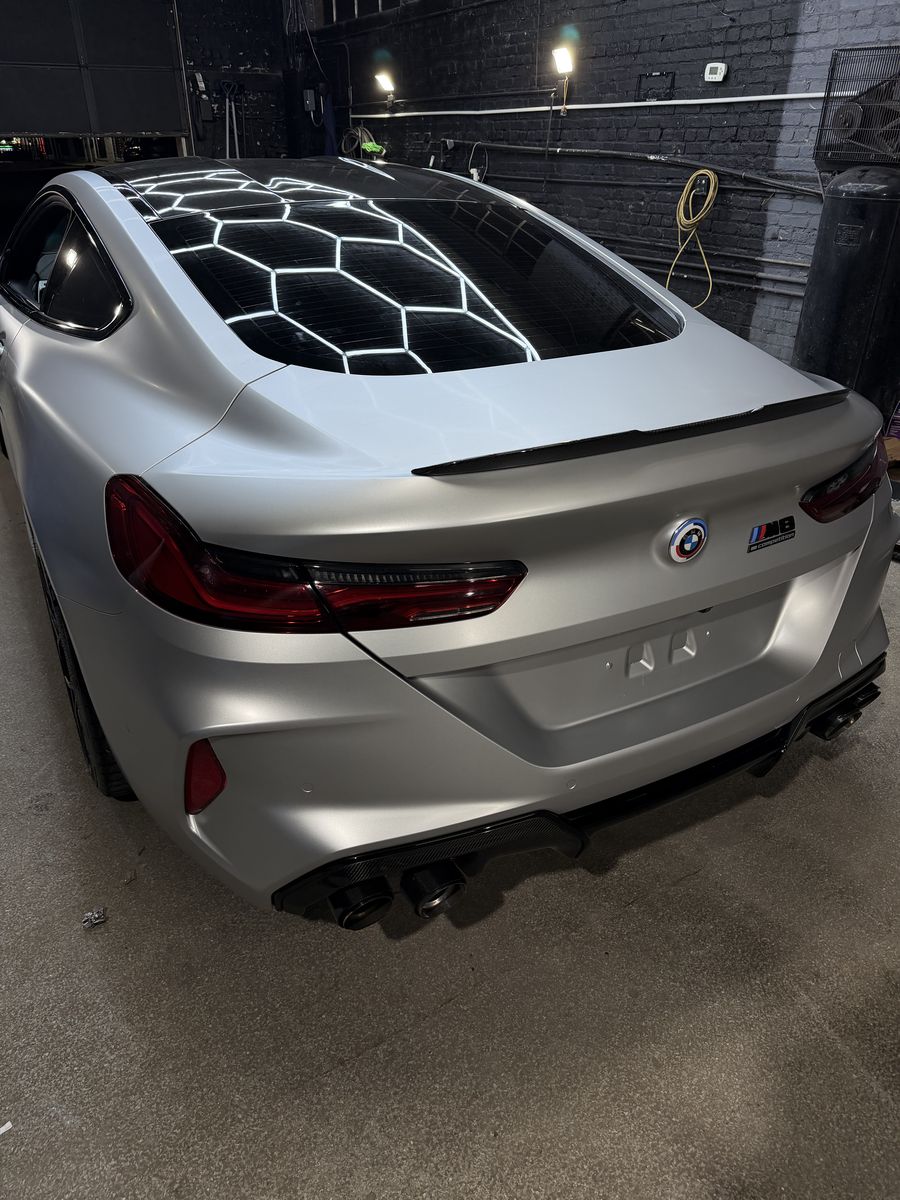 Rear of a BMW M8 in a satin silver wrap, hex lighting across the glass