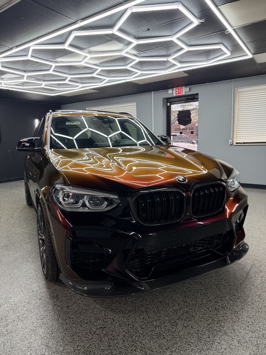 BMW X3 M in a burgundy color shift wrap under the shop lighting