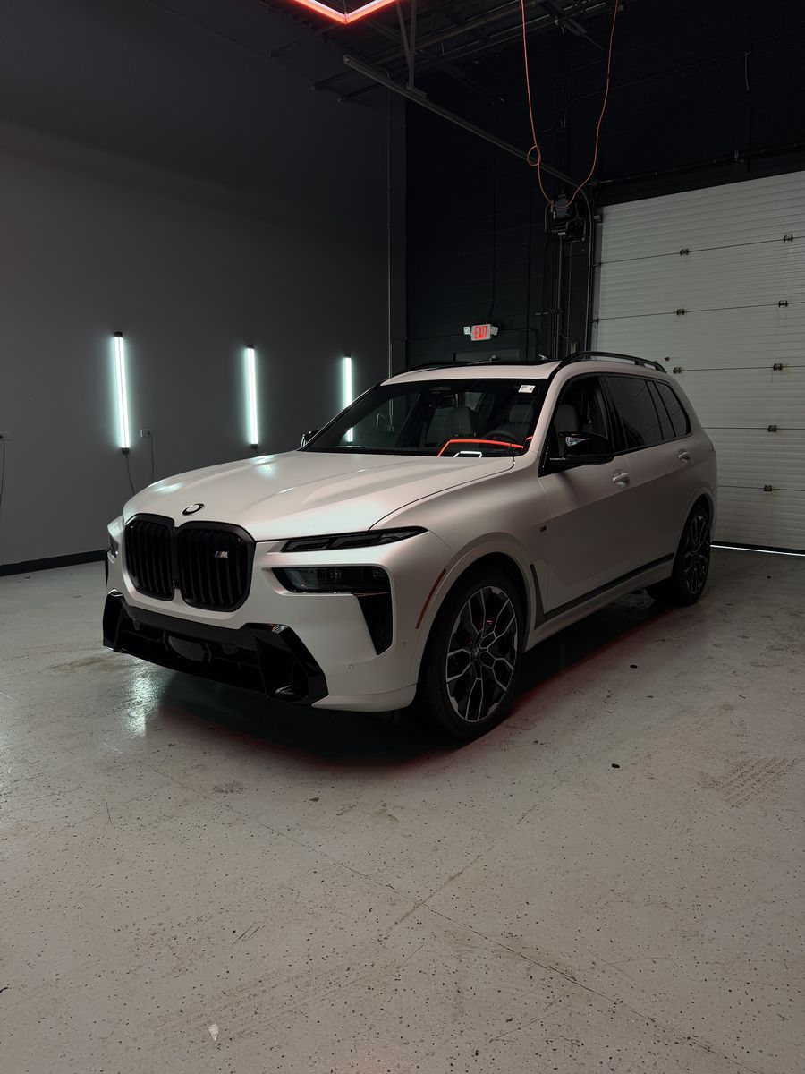BMW X7 M in a white wrap, front three-quarter inside the shop