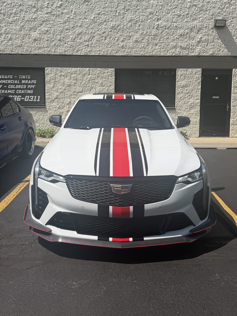 White Cadillac CT4-V Blackwing with red and black racing stripes, head-on outside the Perfect Graphics shop in Cary