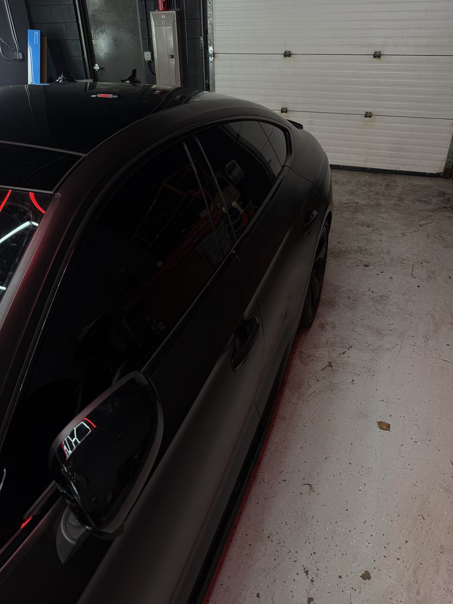 Blacked-out window surround and mirror on a dark coupe inside the shop