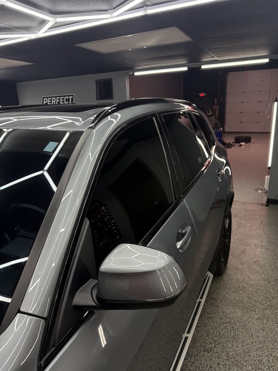 Grey SUV with the window surrounds, pillars and roof rails finished in gloss black, under the shop lights
