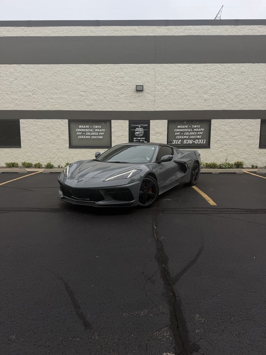 Grey Chevrolet Corvette with tinted glass, parked front-on outside the Perfect Graphics shop