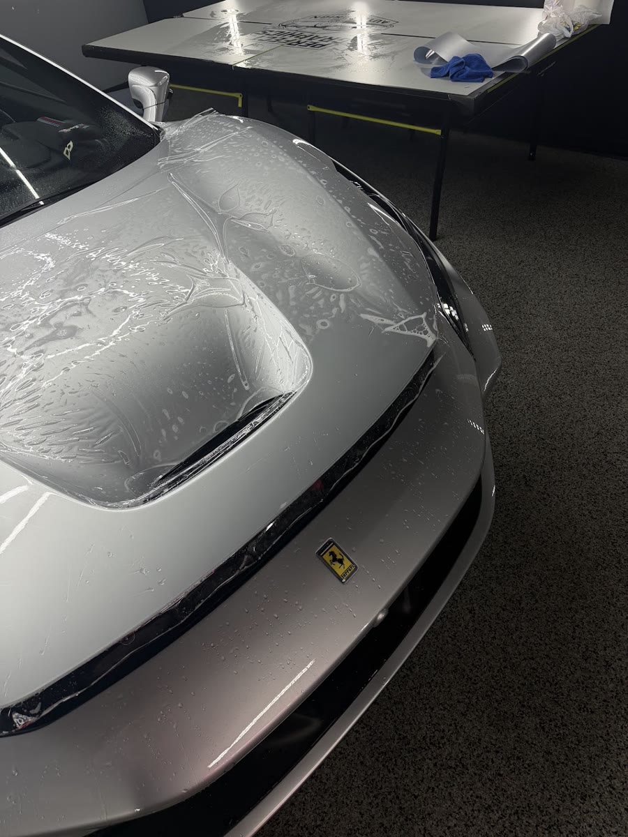 Paint protection film being laid wet across the hood of the silver Ferrari F8