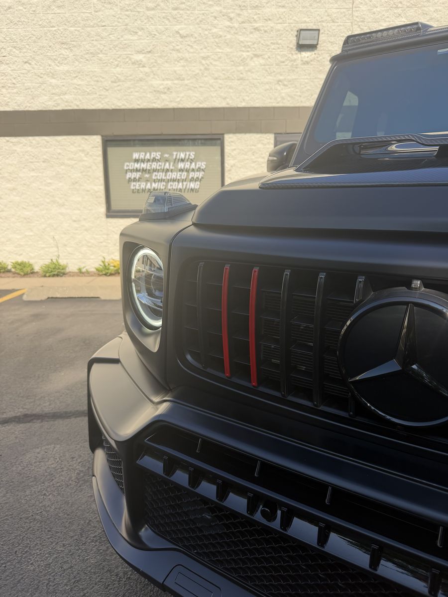 Grille and headlight of a black Mercedes-AMG G-Class with red vertical accents