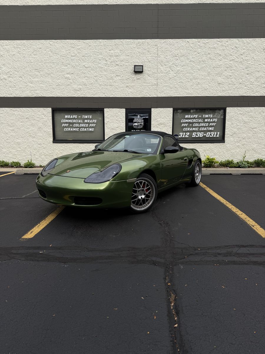 Porsche convertible in an olive green wrap, parked front-on outside the Perfect Graphics shop in Cary