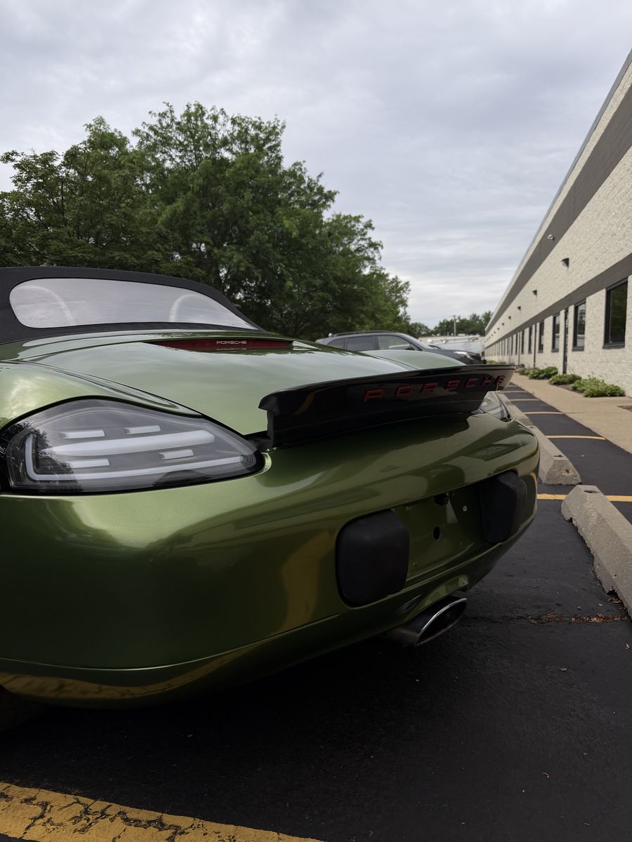 Rear of an olive green wrapped Porsche with the spoiler raised