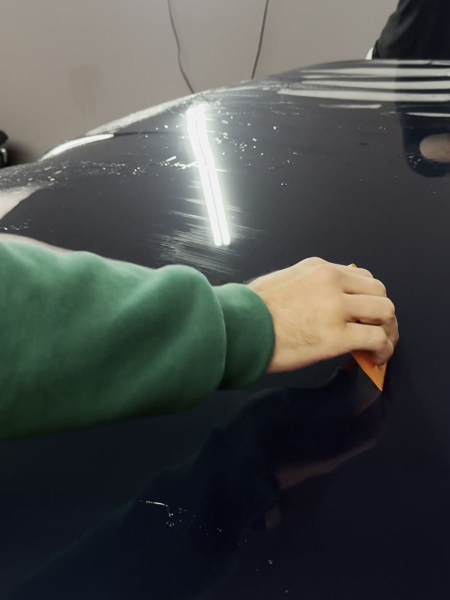 Squeegee pulling the slip solution out from under paint protection film on a dark hood