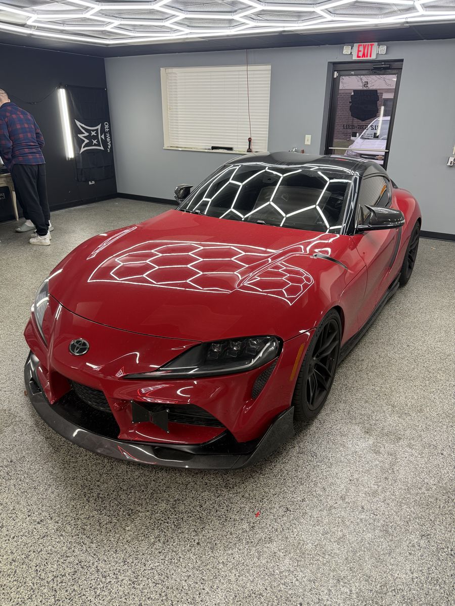 Toyota Supra in a red wrap, front three-quarter inside the shop