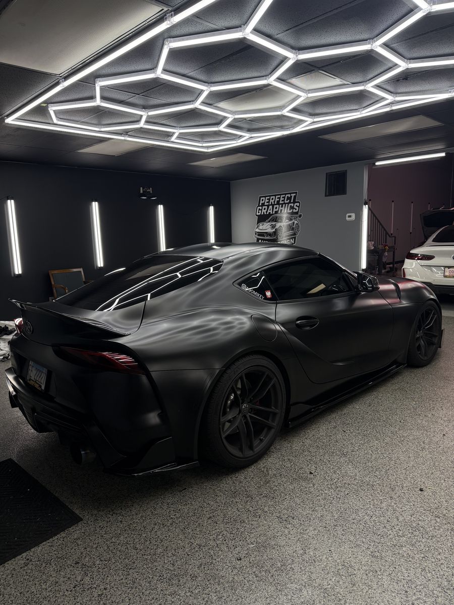 Rear three-quarter of a satin black wrapped Toyota Supra inside the shop
