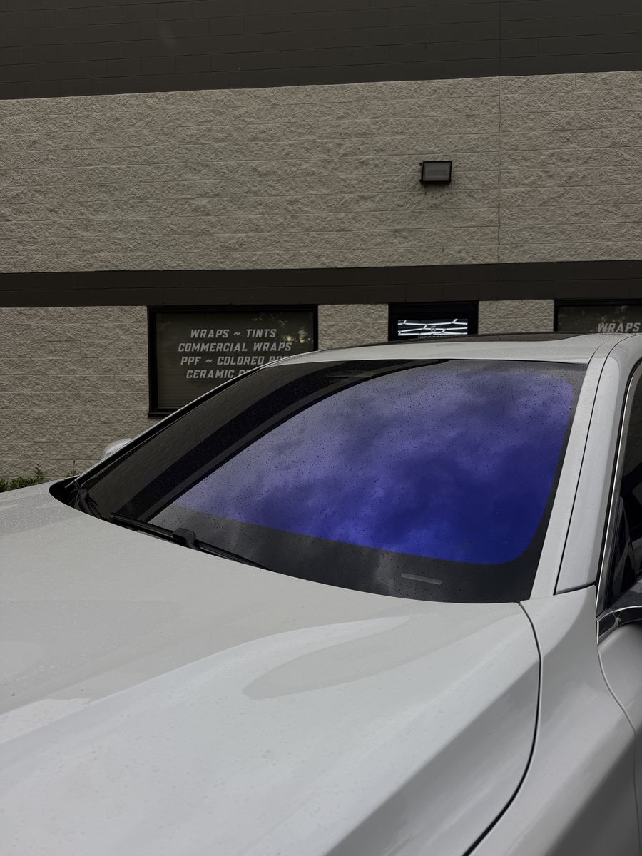 Freshly tinted windshield on a white car outside the shop, the film still curing